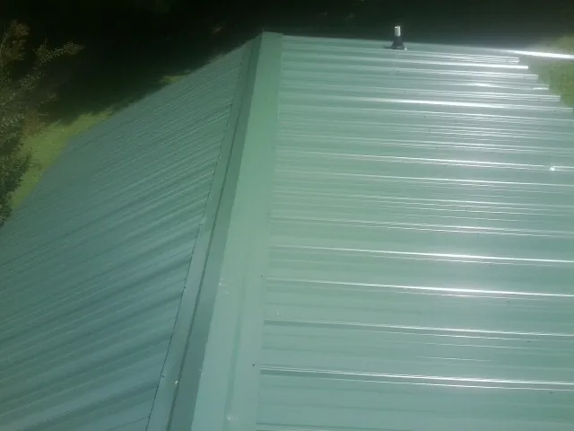 New green metal panels meeting at the ridge of a roof — Flat Roof Repair work by our crew in West Palm Beach
