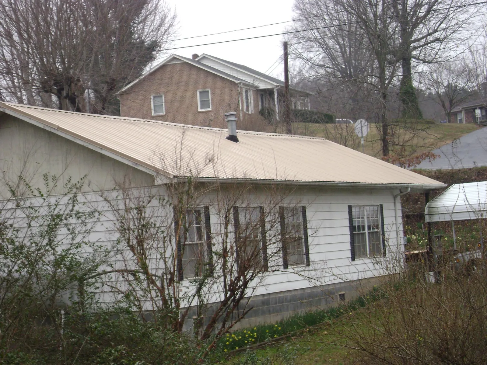 Tan metal roof on a white sided house set into a hillside — Commercial Roofing by Roofing Brothers in West Palm Beach