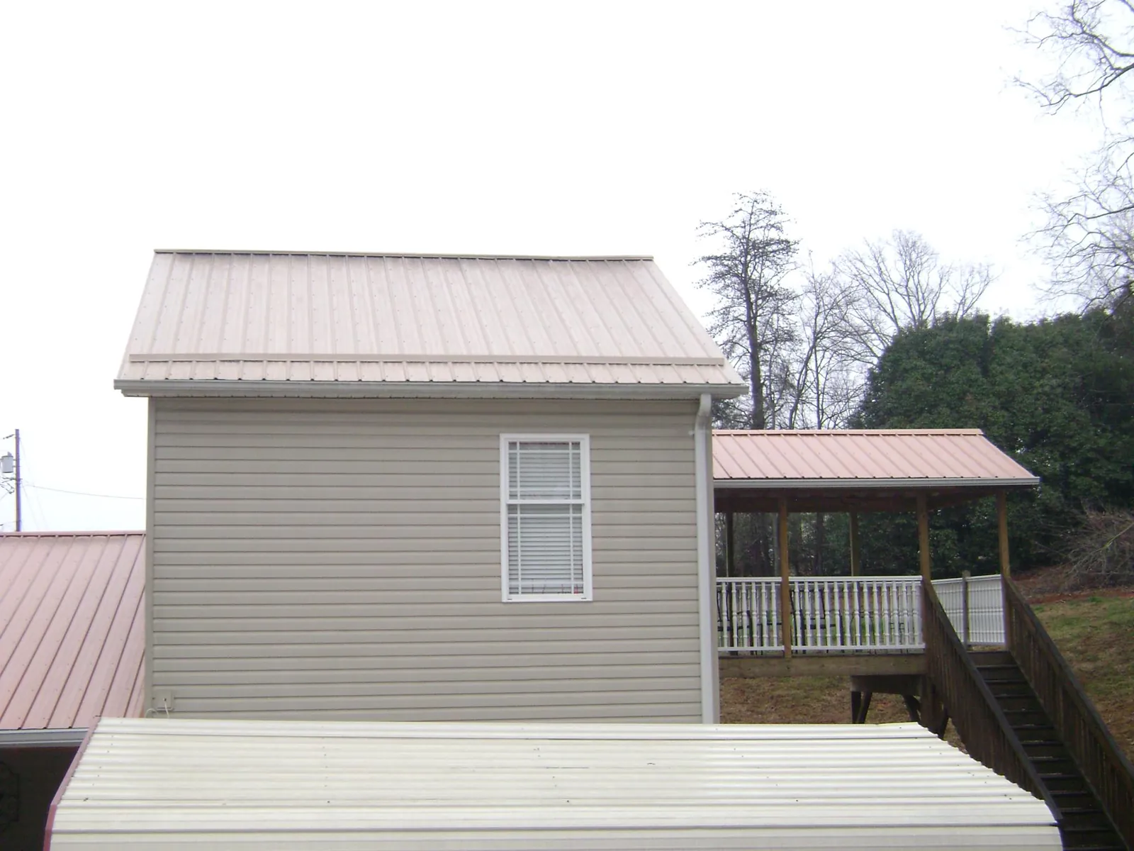 Tan metal roofs on a two story addition and attached porch, from a Roof Replacement job in West Palm Beach